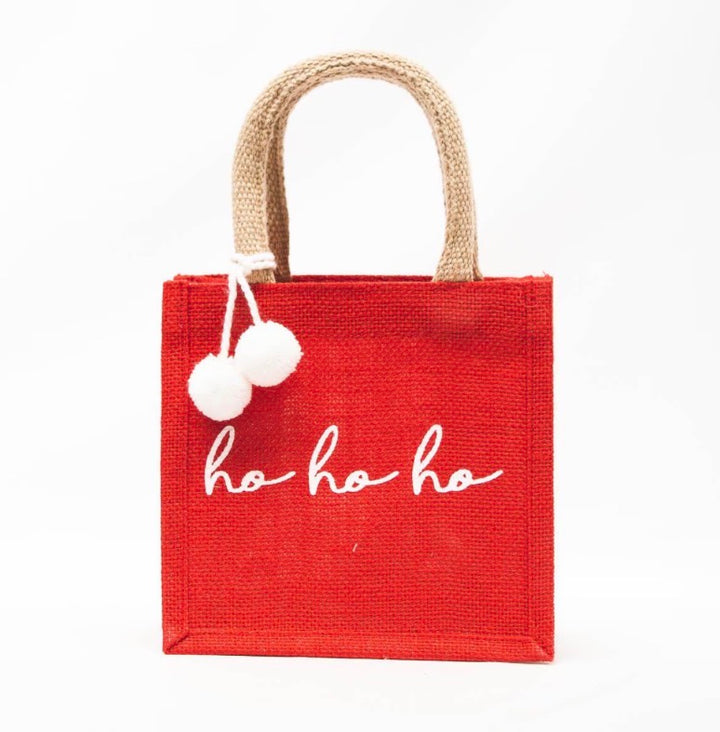 Small red HoHoHo Petite Gift Tote with tan handles, two white pom-poms, and “ho ho ho” in white script. Available in small.