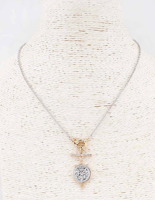 The Silver & Gold Cove Necklace features a silver chain, gold toggle clasp, and round textured silver pendant. Available in 16″, 18″, and 20″ lengths.