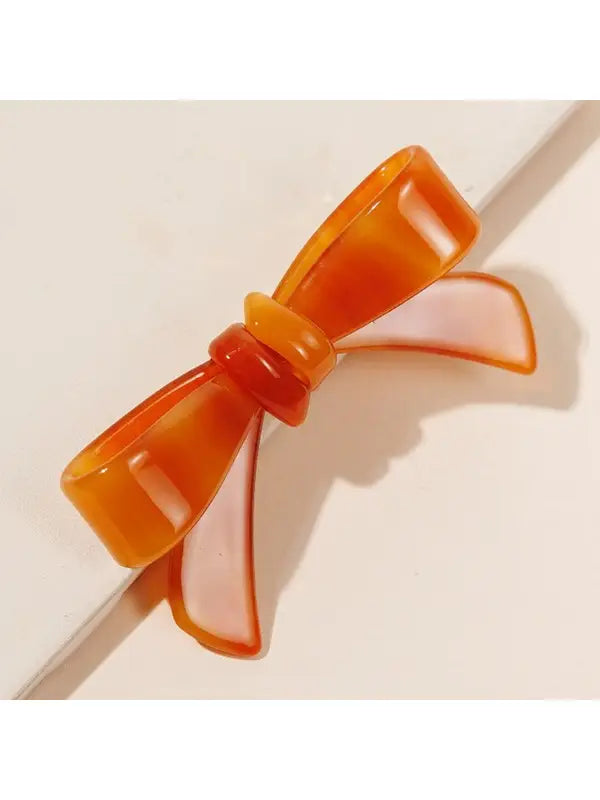 Shiny Bow Acrylic Alligator Hair Clip shaped like a bow, featuring a gradient from dark orange edges to lighter translucent center. Available sizes: Small, Medium.