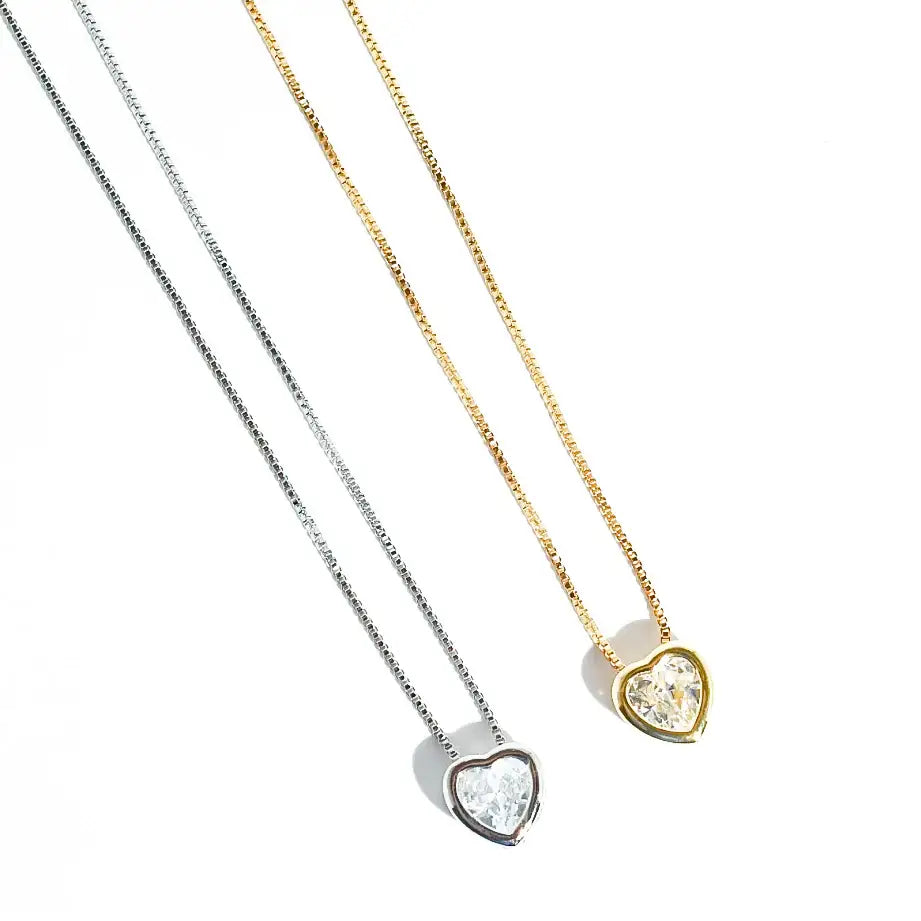 The Tiny Love Necklace: Silver has a heart-cut crystal and clear gemstone on a silver chain. Available sizes: 16", 18".