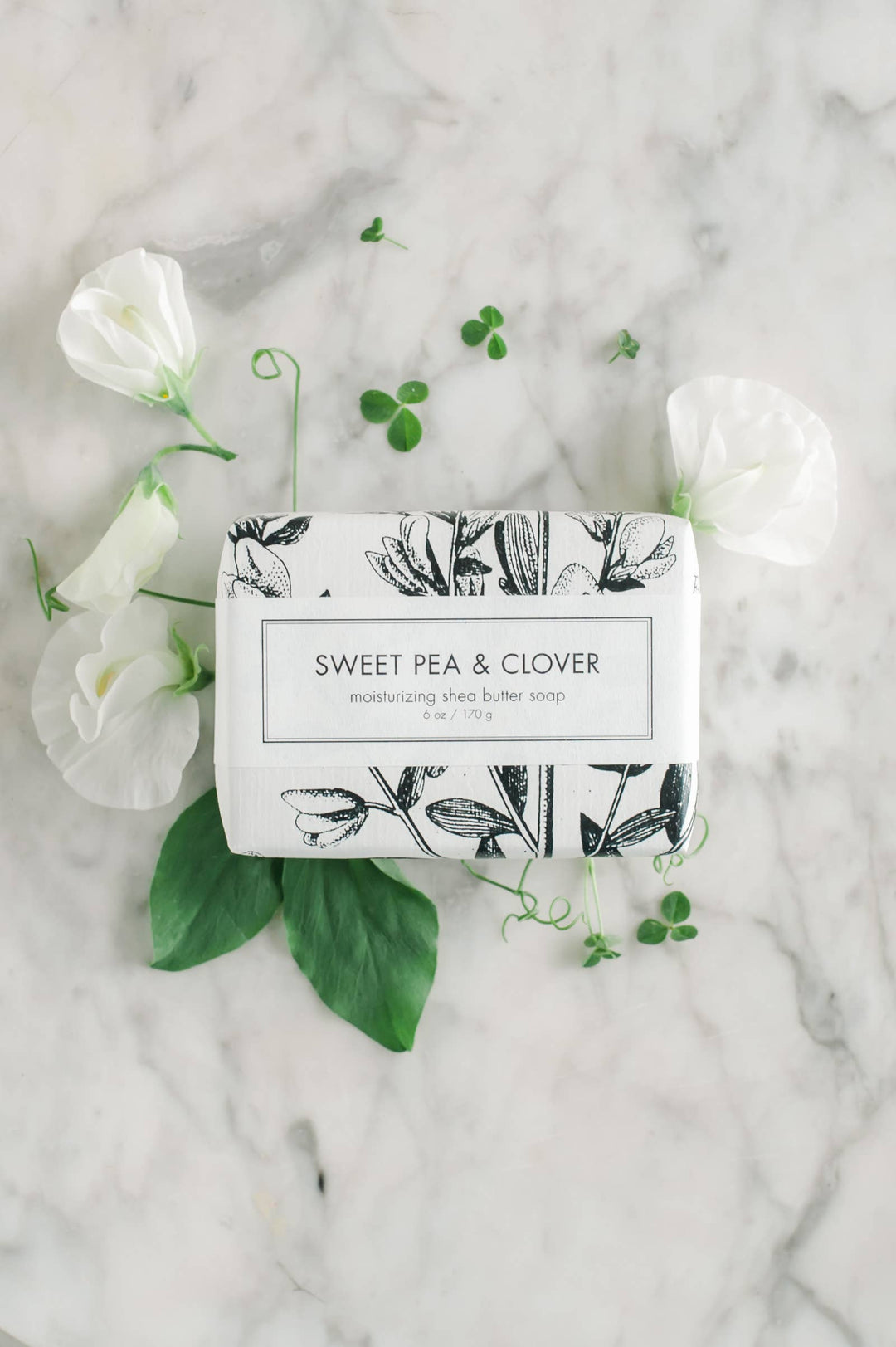 A Sweet Pea &amp; Clover soap bath bar, presented in an eye-catching black and white floral wrapper. Delicately scented with refreshing sweet pea and clover notes. Arrives elegantly placed atop a chic marble surface for an enhanced aesthetic appeal.