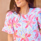 Cassidy Hibiscus Harmony White Top with pink floral print, ruffled sleeves, crew neck. Available in XS-XL.