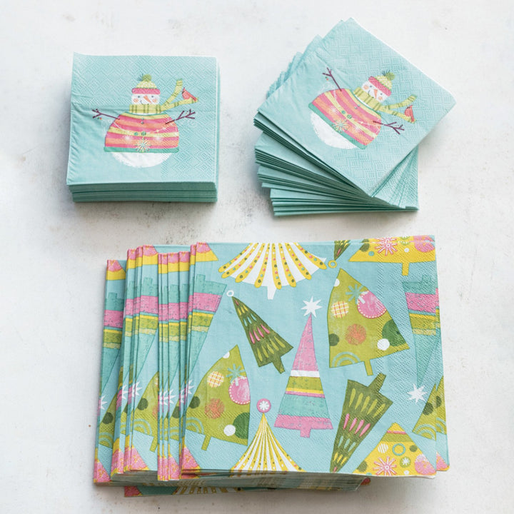 Light blue square paper napkins with Christmas tree and snowman patterns.