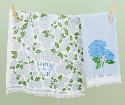 Two-pack towels: blue hydrangea floral print and light blue embroidered design. Available in standard kitchen towel size.