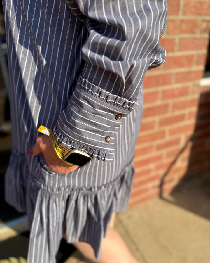 Drop Waist Shift Dress in blue and white stripes, featuring brown sleeve buttons and a ruffled hem. Available in sizes XS–XL.