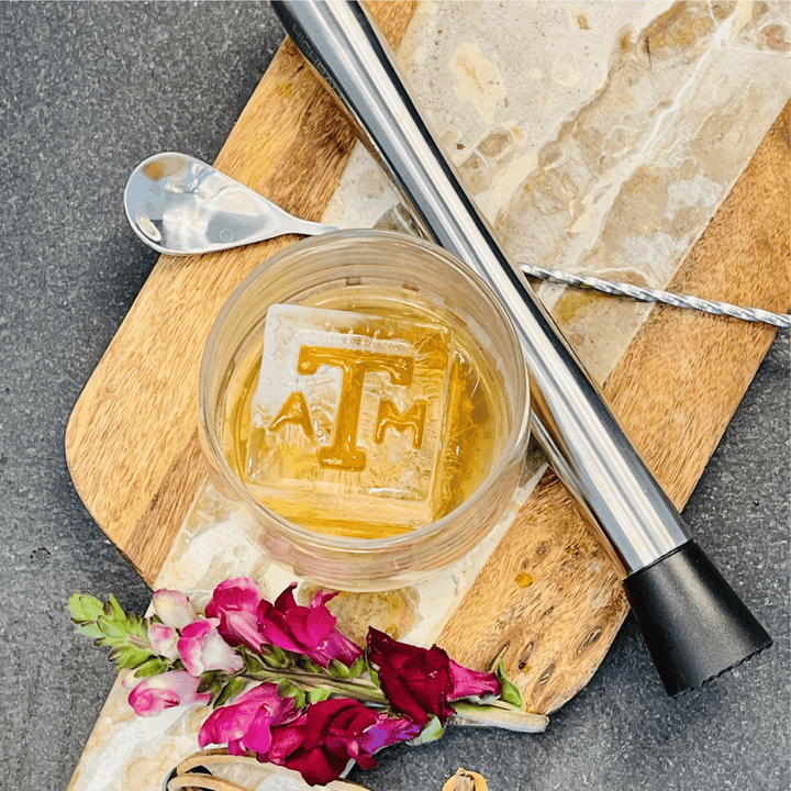 A glass of amber liquid with a large, clear ice cube featuring Texas A&amp;M Block ATM Inserts - 3 Pack embossed with the letters ATM.