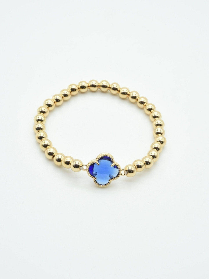 Gold beaded bracelet with central blue crystal clover charm. Available in S, M, and L sizes.