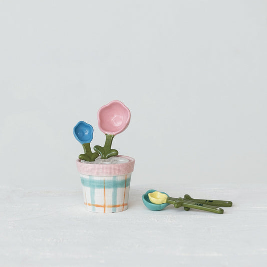 Hand-painted stoneware measuring spoons with green stems and checkered pot holder; available in standard measuring sizes.