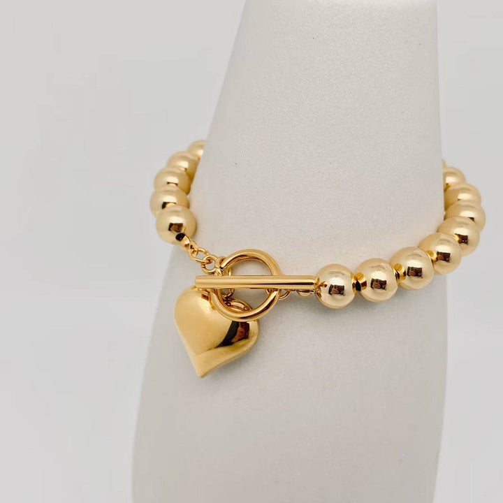 18K gold-plated bracelet with 8MM beads, heart charm, and T-bar clasp in stainless steel. Available in multiple sizes.