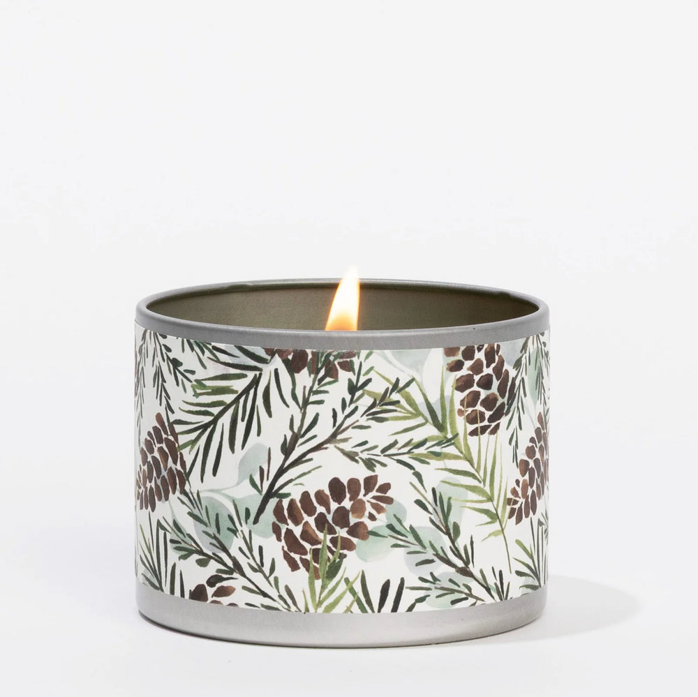 Lit 4oz Silver Spruce candle in a metal tin with a pinecone and evergreen branch pattern.