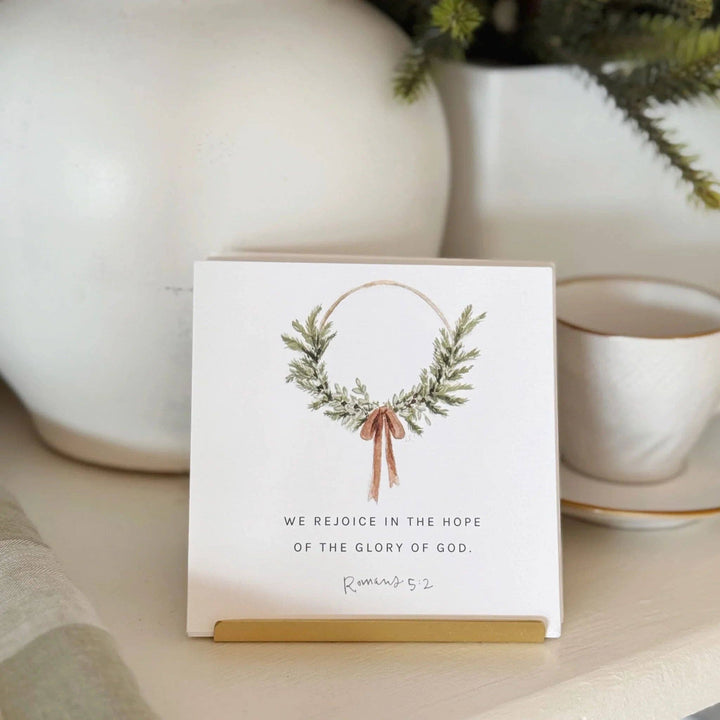 Christmas card with watercolor wreath and pink bow, "We rejoice in the hope of the glory of God." Sizes available.