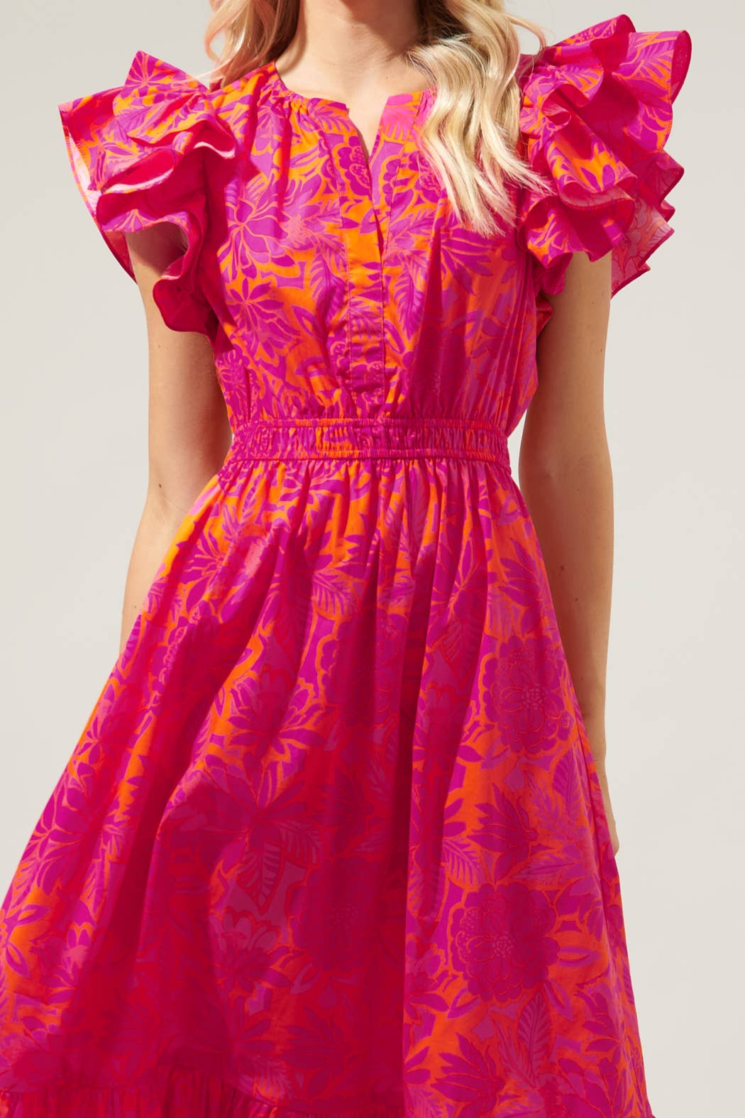 The Bali Tropics Jelina Ruffle Sleeve Midi Dress is a bright pink dress characterized by an appealing tropical print. The design features ruffle-tiered skirt, adding a flirty touch to the overall look. This midi length dress is available in various sizes.