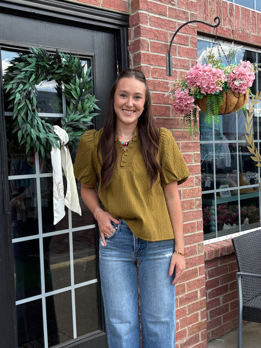 Olive ruffled blouse with a relaxed silhouette, available in sizes XS–XL.