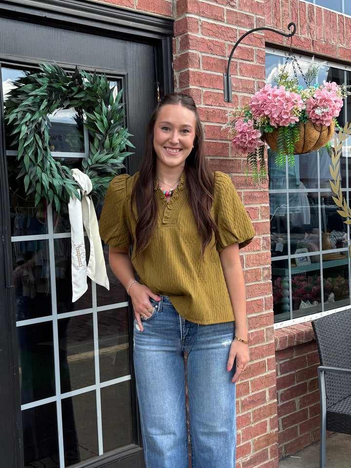 Olive ruffled blouse with a relaxed silhouette, available in sizes XS–XL.