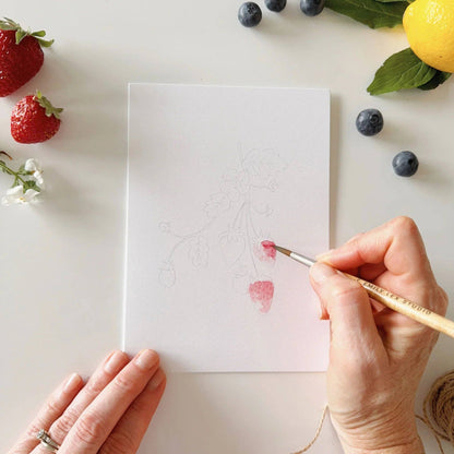 Fruit paintable watercolor notecard set shown with a hand painting a strawberry illustration. Available in 4x6 and 5x7 inch sizes.