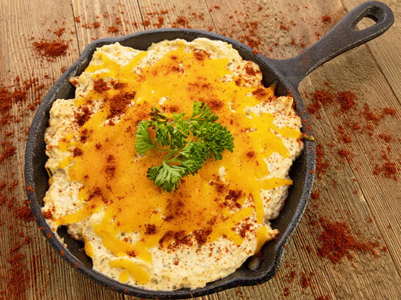 Baked Enchilada Dip Mix in a skillet, topped with melted cheddar, paprika, and parsley; available in 8oz and 16oz sizes.