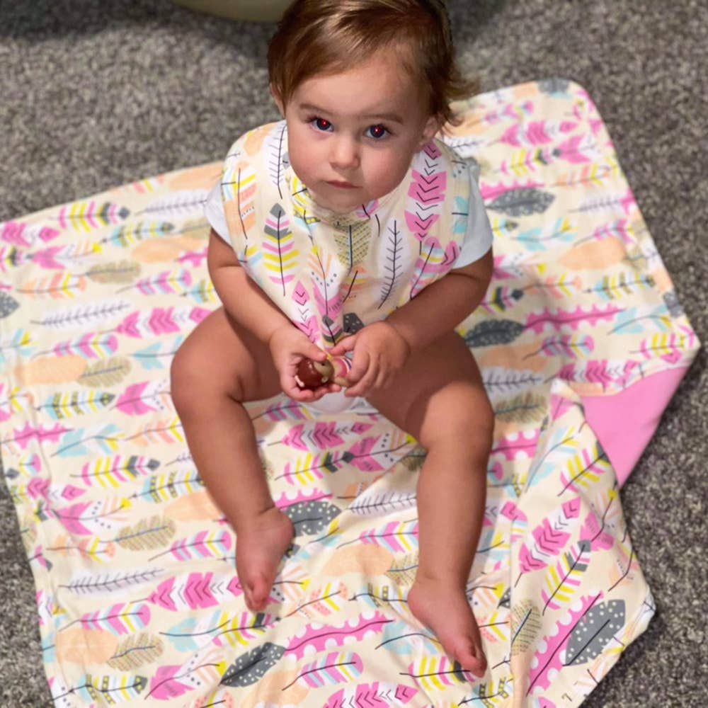 A toddler sits on a Pink Floral Blanket+Bib Baby Shower Gift Set, holding a small object, with a curious expression.