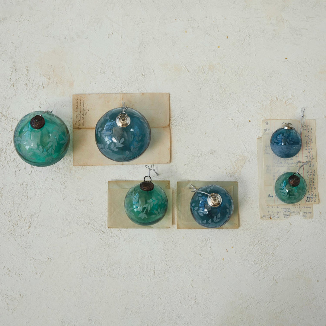 Five recycled glass ball ornaments in blue and green, featuring etched leaf patterns and metallic caps.