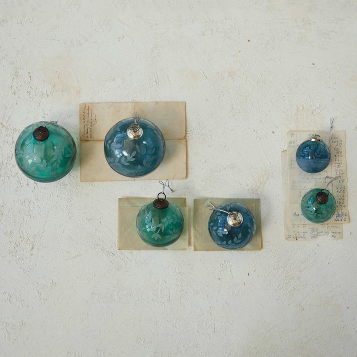 Five recycled glass ball ornaments in blue and green, featuring etched leaf patterns and metallic caps.