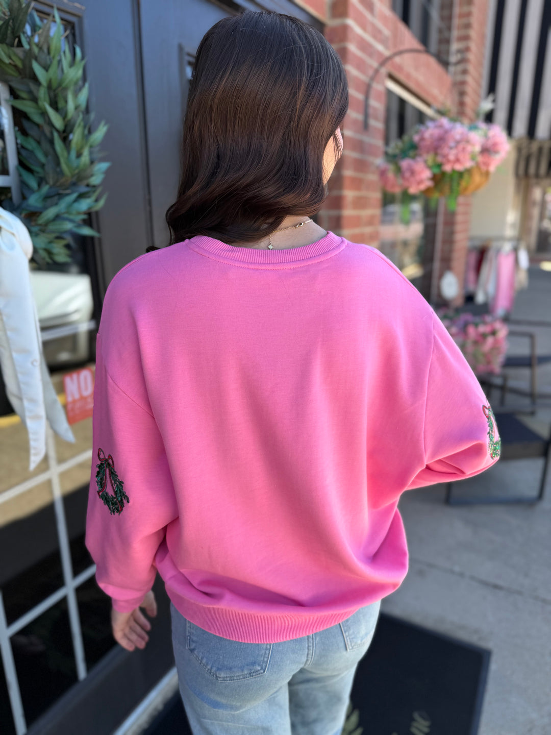 Bright pink Sarah Joy Wreath sweatshirt with embroidered Christmas wreath sleeve details. Available in all sizes.