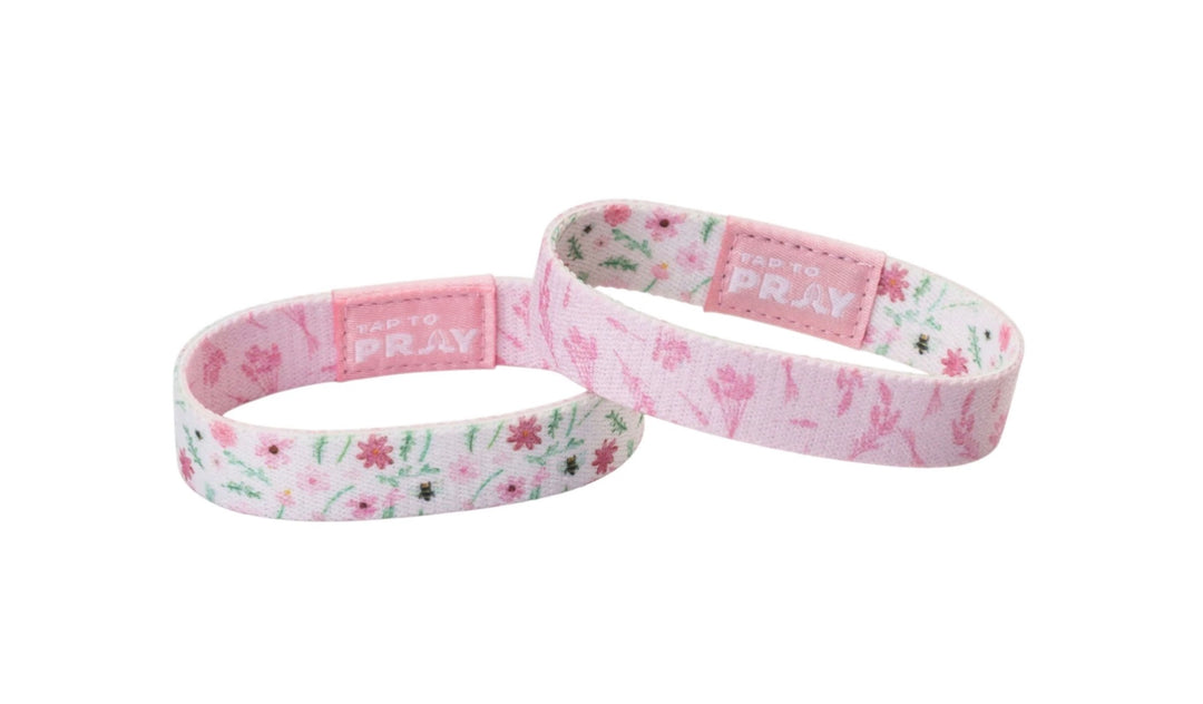 Two pink floral Tap To Pray™ Meadows wristbands with rectangular embossed prayer tags.