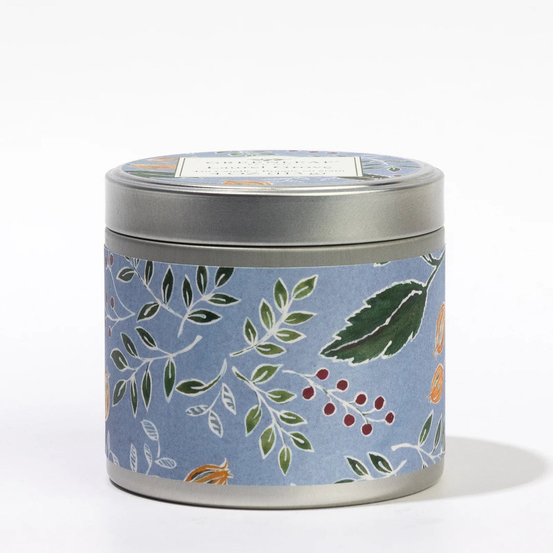 Round 4oz Laurel Grove candle tin with a blue label featuring green, orange, and red botanical design; matching lid with white label.