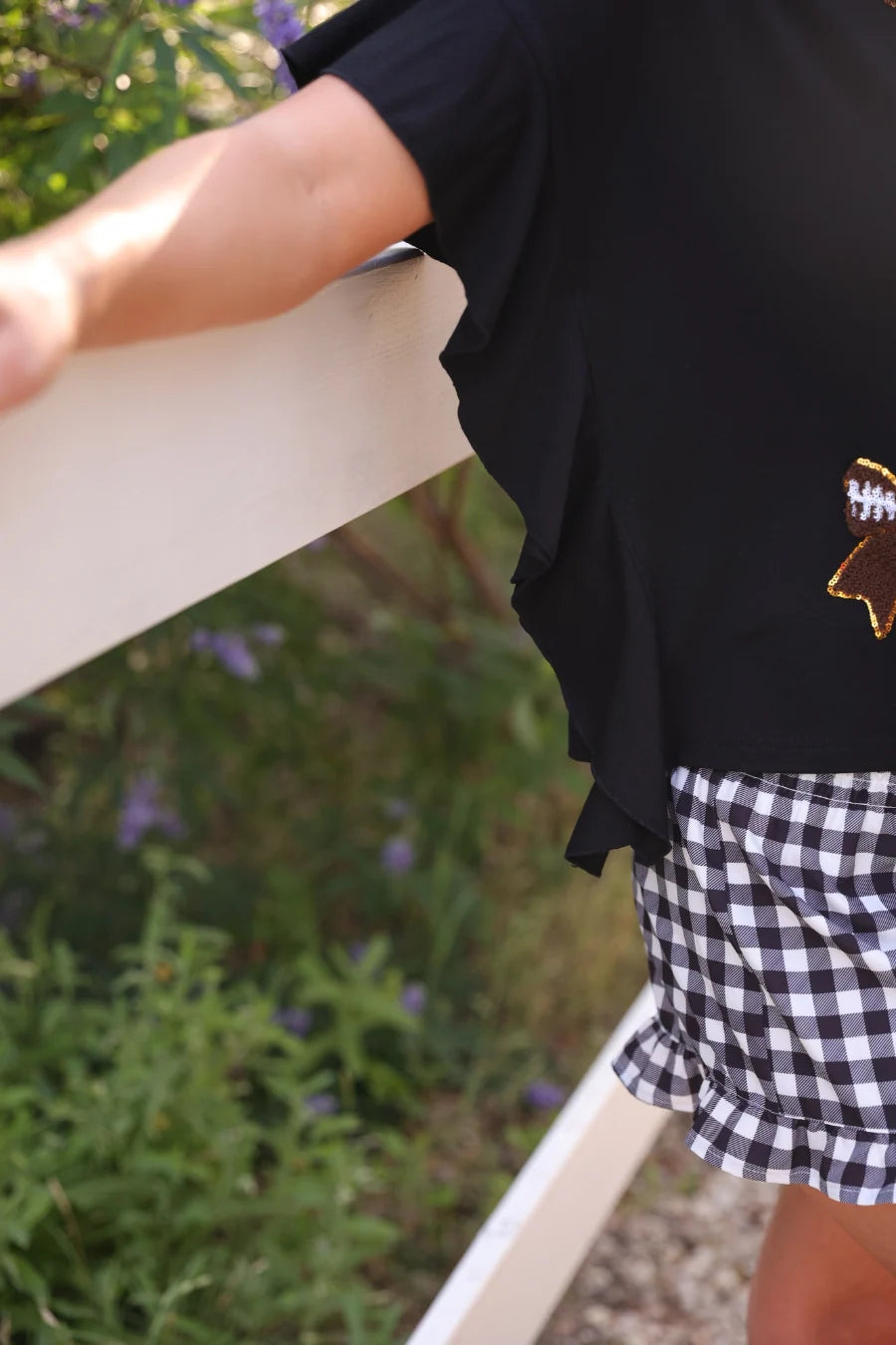 Sideline Sparkle Ruffle Top with football bow patch detail, paired with checkered shorts. Available in sizes 2T-6.
