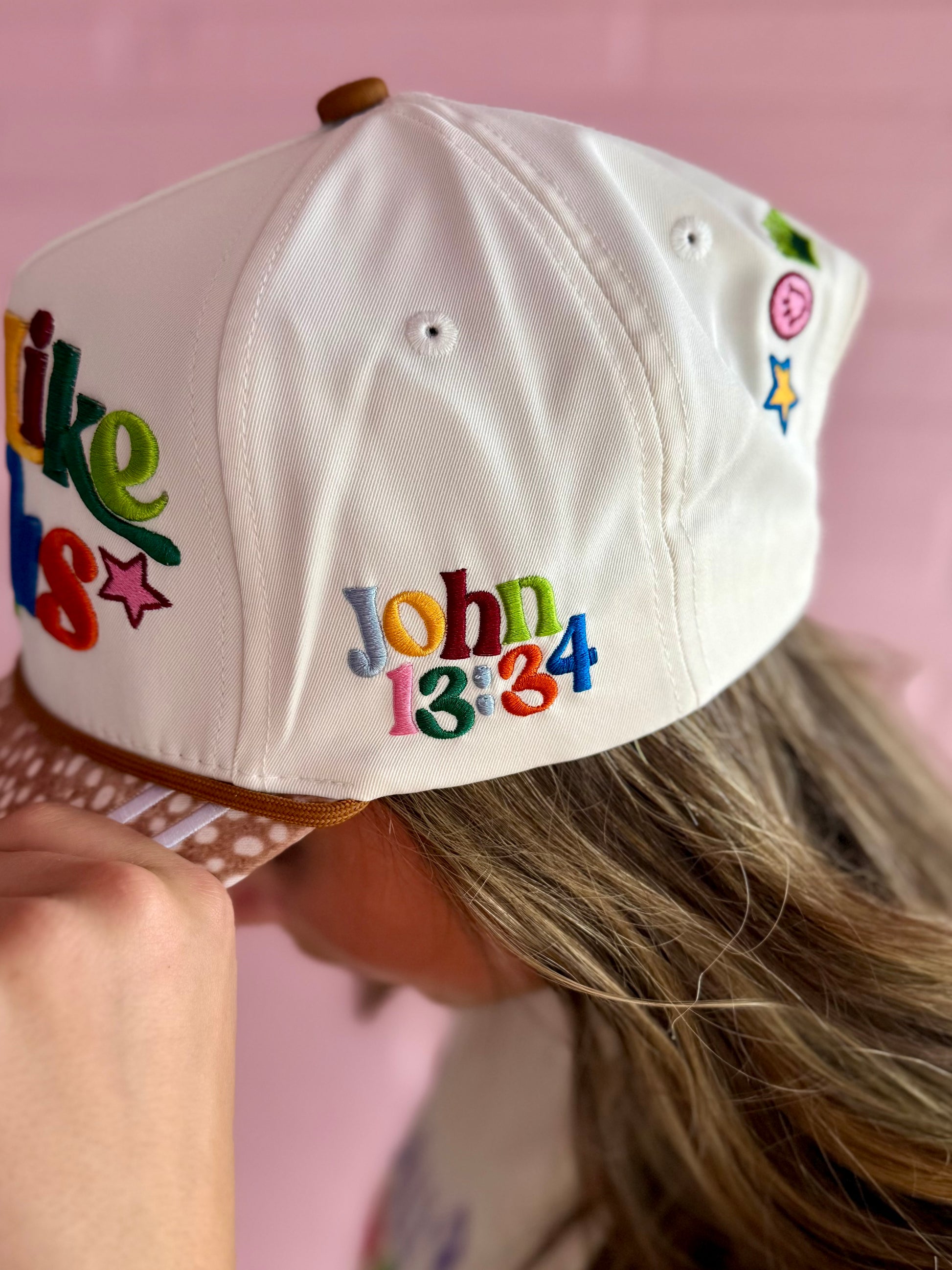 White embroidered Love Like Jesus Hat with colorful “John 13:34” text, vibrant letters, and symbols. Sizes: S, M, L.