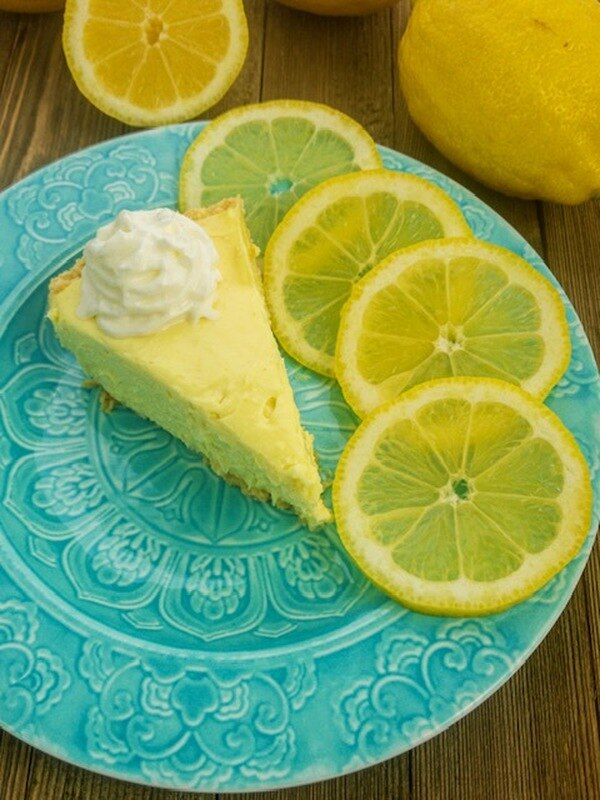 Lemon Ice Box Cheesecake Dip on a blue plate, topped with whipped cream and four lemon slices. Sizes available: single serving.
