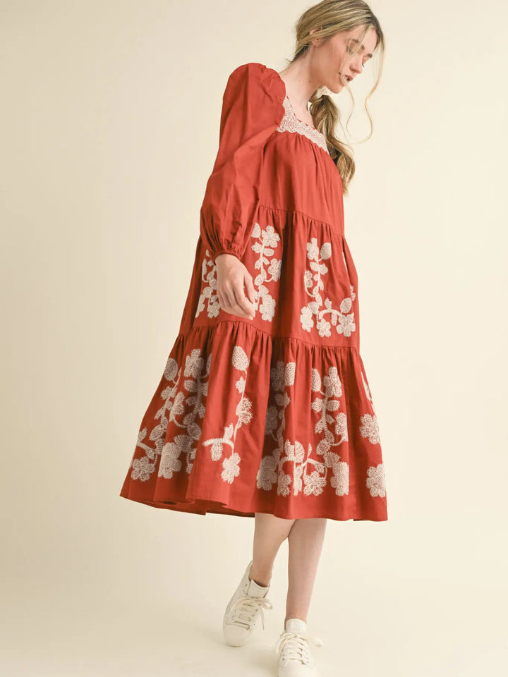 Rust midi dress with square neckline, long sleeves, and white floral embroidery. Available in all sizes.