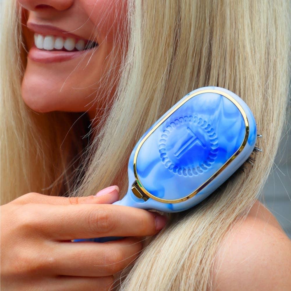 Tide & True Mini Boar Brush, a compact blue and white travel brush with a circular design and letter “T” in the center. Available in mini size.