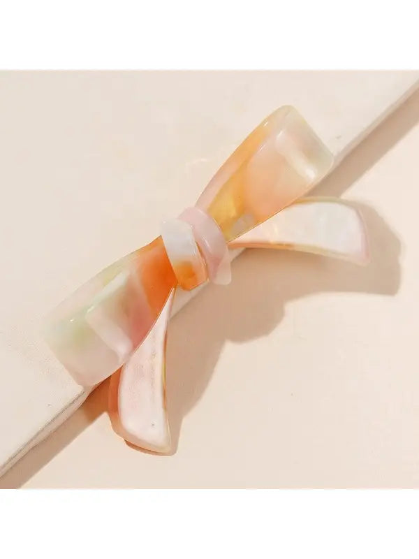 A Shiny Bow Acrylic Alligator Hair Clip shaped like a bow with a mix of pastel colors, including pink, peach, and cream. Glossy finish for an elegant appearance. Sizes available: Small, Medium, Large.