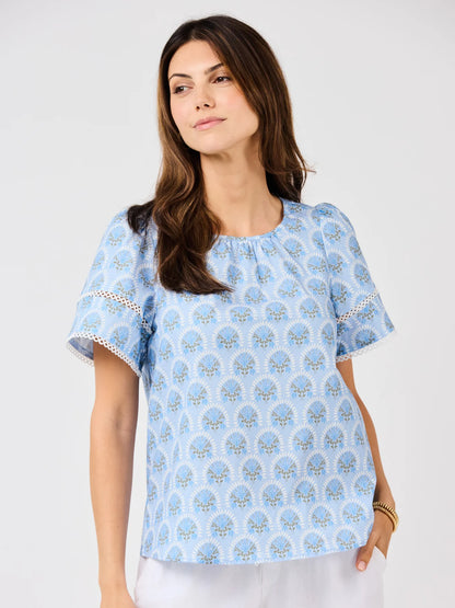 Tabby Sunshower Flora Blue Top with white and yellow floral pattern, eyelet-detailed sleeves. Available in XS–XL.