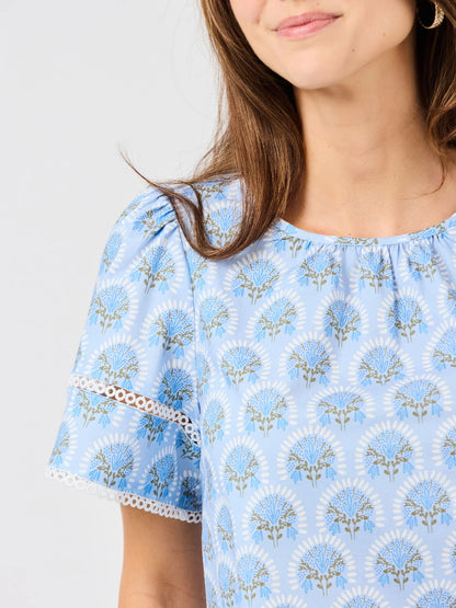 Tabby Sunshower Flora Blue Top with blue floral pattern, flutter sleeves, white eyelet detail. Available in sizes XS-XL.