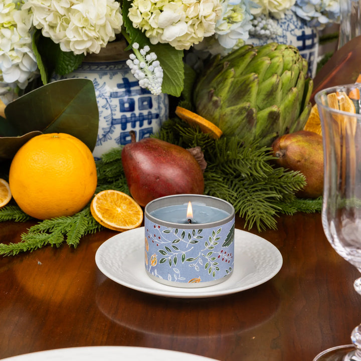 A blue 4oz Laurel Grove candle with a subtle fir balsam scent, lit on a white plate.