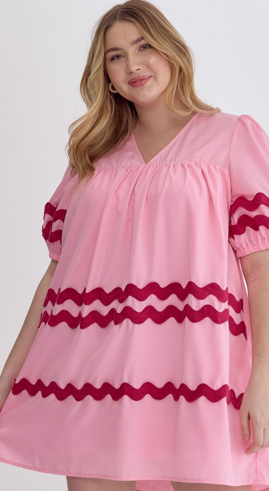 The Bay Ribbon Dress features ruffle sleeves and a wavy red rick rack trimming around the midsection. Sizes available are small, medium, large, and extra-large.