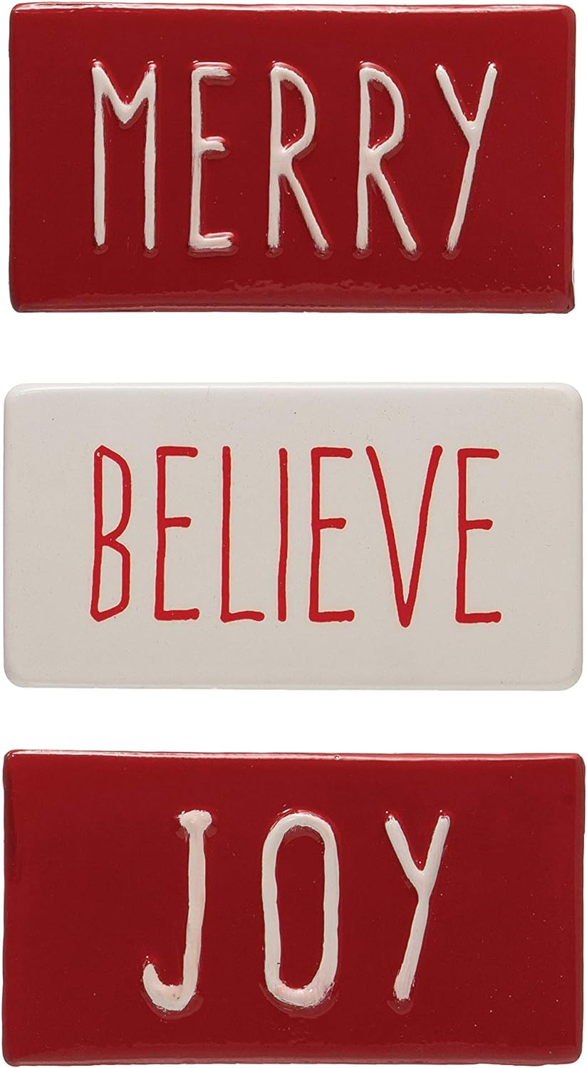 Three rectangular red and white metal signs reading “MERRY,” “BELIEVE,” and “JOY.”.