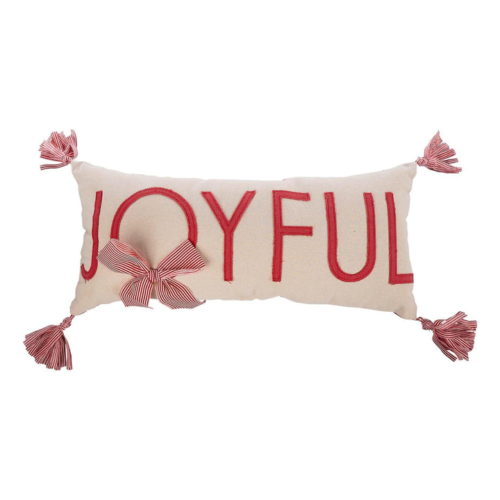 Rectangular cream-colored Joyful Pillow with red “JOYFUL” embroidery, a red and white striped bow on the O, and matching corner tassels.