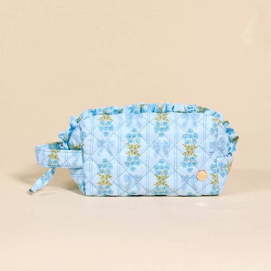 Light blue floral quilted pouch with ruffled trim, side handle, gold emblem, and wipeable interior. Sizes: Standard.
