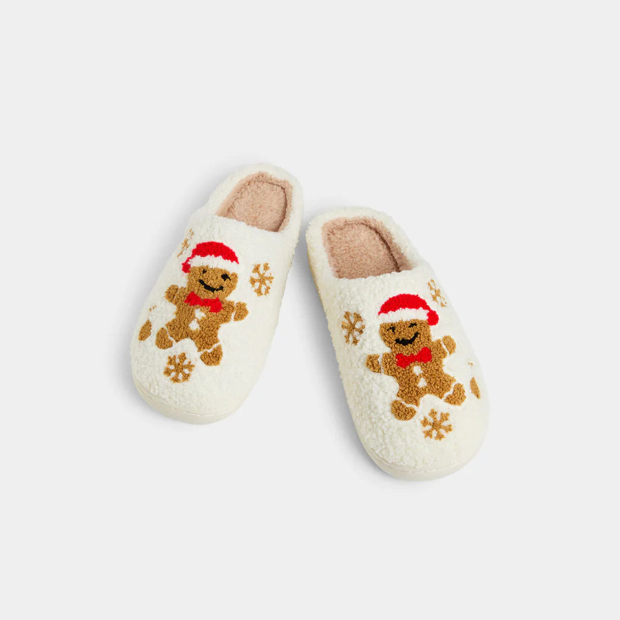 Cream-colored fuzzy Happy Feet Gingerbread Man slippers with Santa hat, red bowtie, and snowflake designs. Available in multiple sizes.