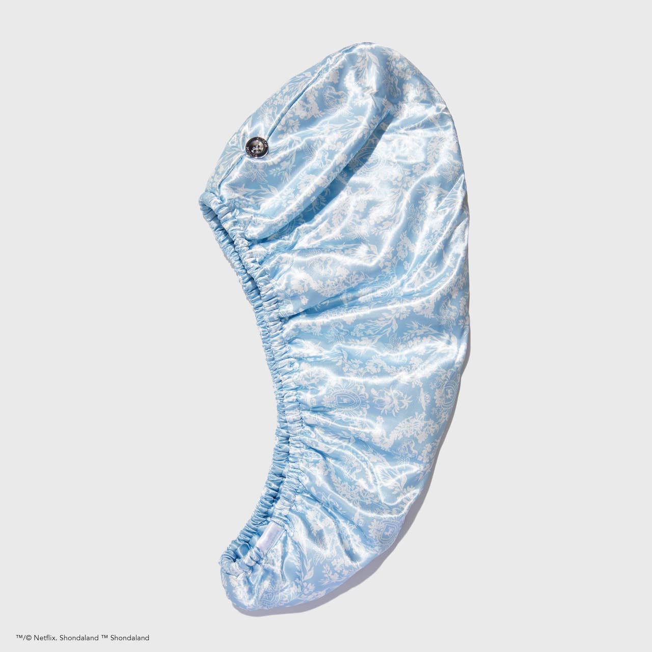 Light blue satin hair towel with subtle floral print and elastic edges; available in one size; reduces frizz.