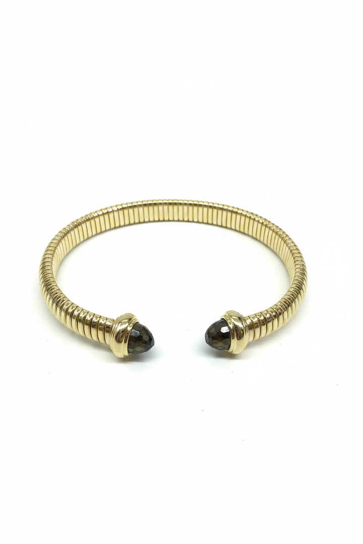 Gold cuff bracelet with ribbed texture, two dark rounded gemstone ends. Available in S, M, and L.