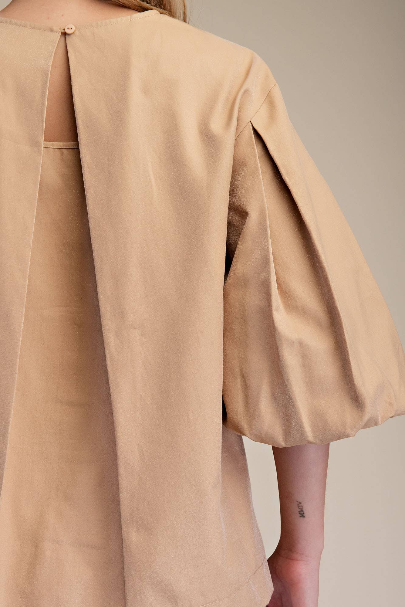 Taupe round neck puff sleeve top with fine pleats, lightweight fabric, and keyhole back. Available in sizes XS-XL.