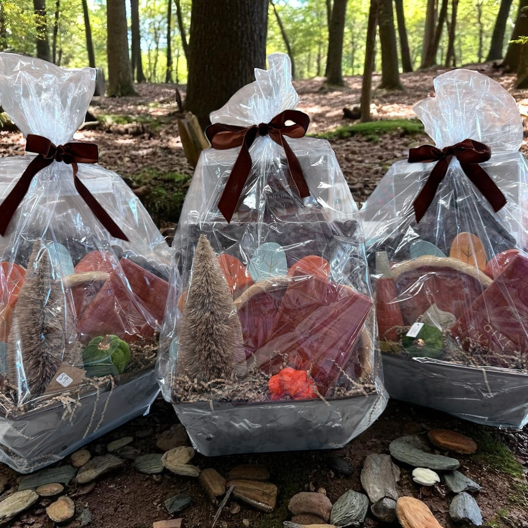 Three Thanksgiving Baskets, wrapped in clear cellophane with brown ribbons and filled with assorted colorful items and small faux trees. Available in small, medium, and large sizes.