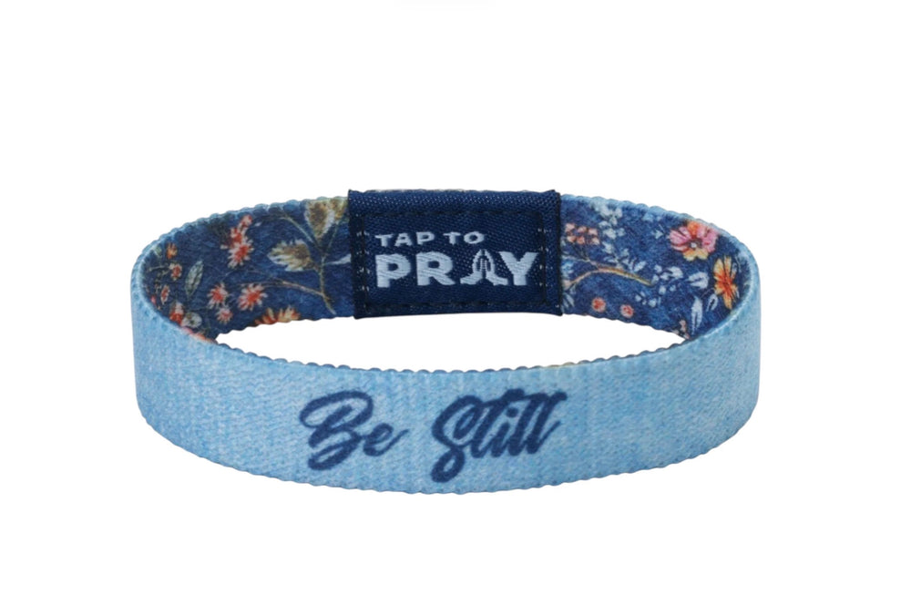 Light blue elastic Tap To Pray™ Wristbands - Wildflower featuring “Be Still” text, patterned interior, and “Tap to Pray” tag with praying hands icon.