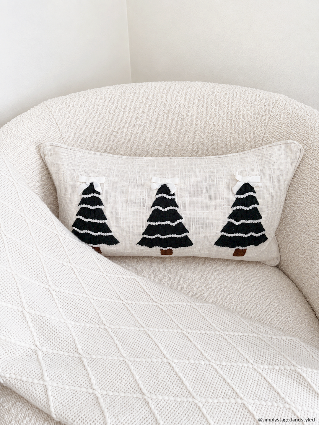 White velvet lumbar pillow featuring three black crewel embroidered Christmas trees with small white bows.