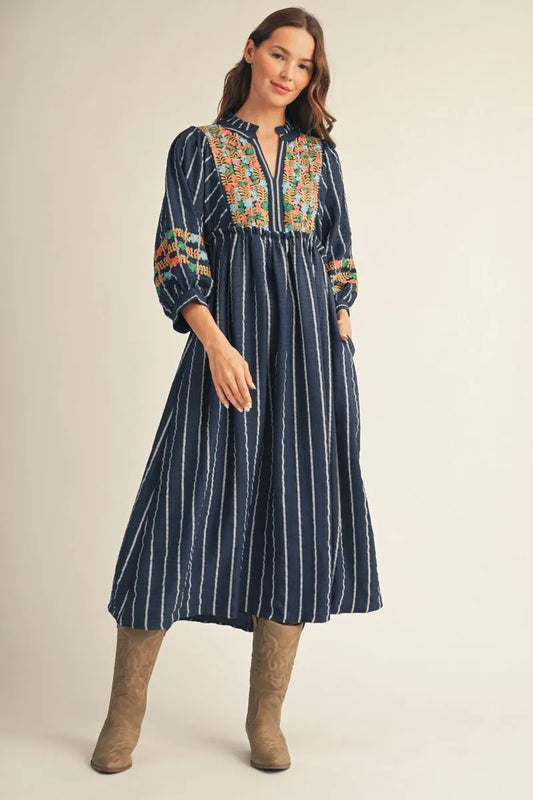 Floral Embroidered Midi Dress: navy blue, long sleeves, ankle length, colorful floral embroidery on bodice and sleeves, ruffled neckline, vertical white stripes. Available in sizes XS–XL.