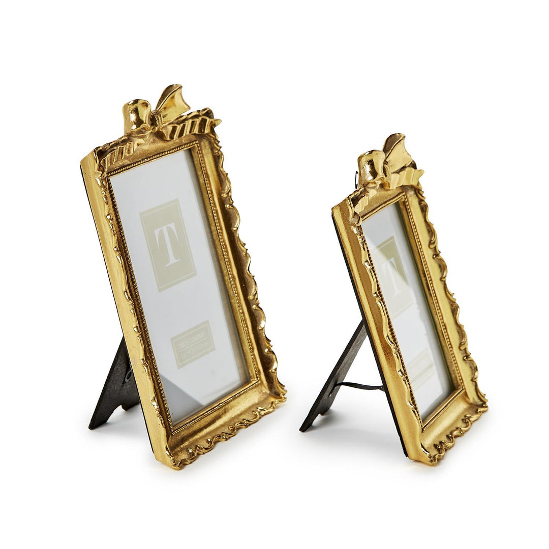 Set of two gold photo frames with decorative bows, black easel backs; sizes: one small, one slightly larger.