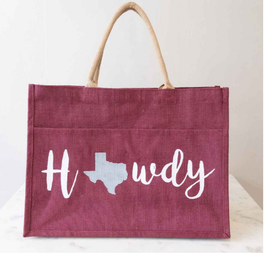 Red Howdy Jute Tote with beige handles. Features "Howdy" in white, with a light blue Texas silhouette as the "o". Sturdy and perfect for daily use. Available sizes: Small, Medium, Large.