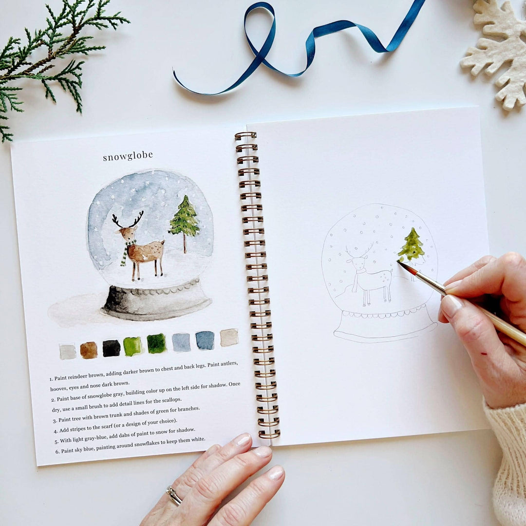 Winter watercolor workbook showing a finished snowglobe and step-by-step painting instructions.